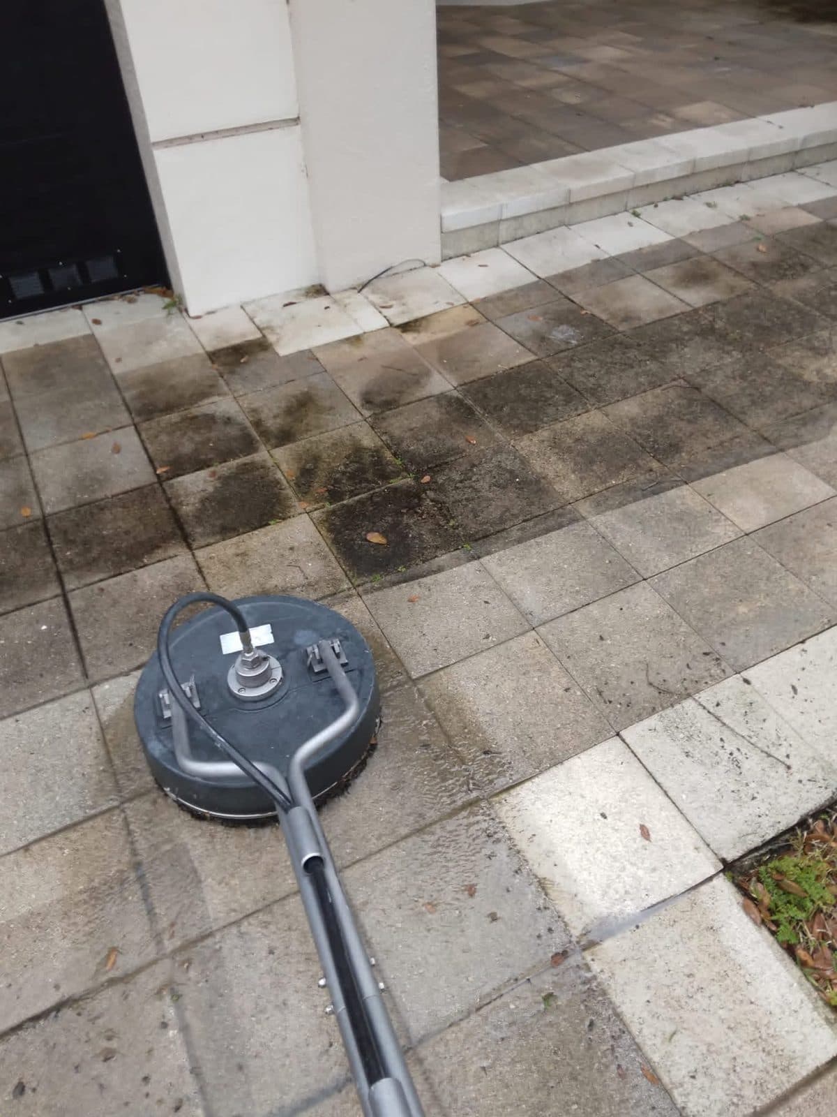 Surface cleaner halfway across a paver driveway, one side black with algae and the other clean